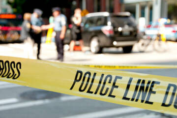 Police line at a crime scene with unrecognizable officers and vehicles in the background.